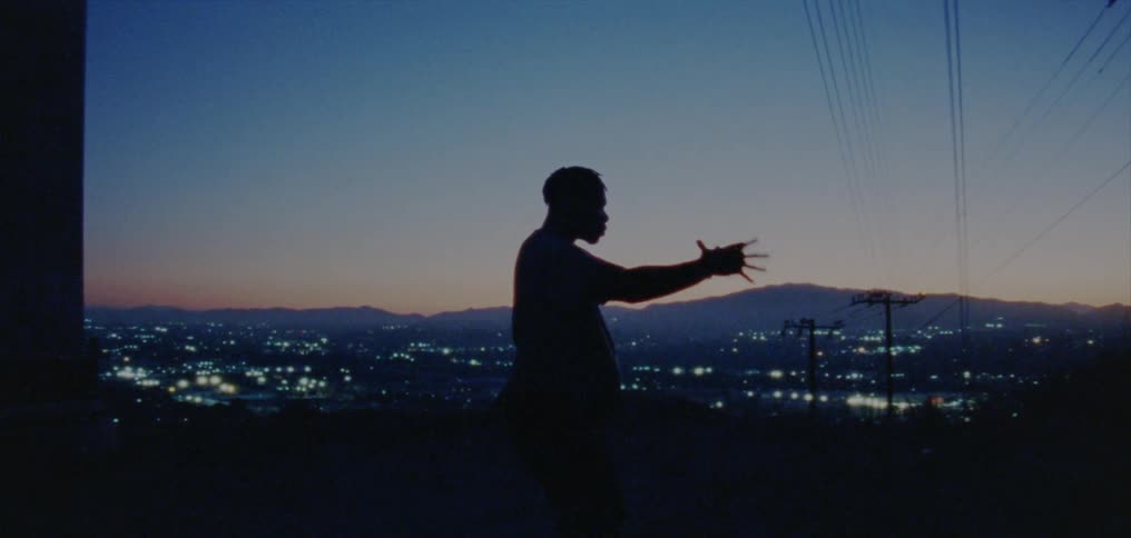 The silhouette of a young man dancing on a ridge overlooking city lights
