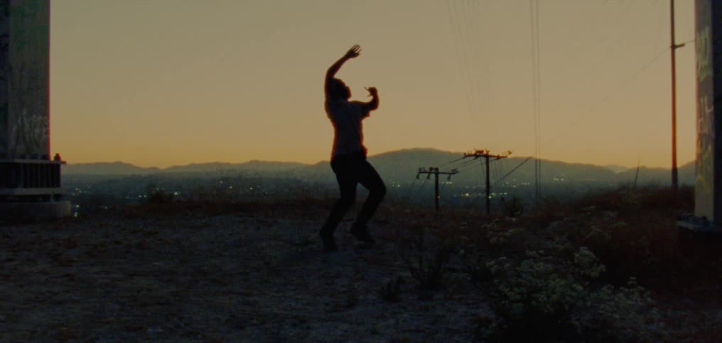 The silhouette of a young man dancing on a hill with a golden sky