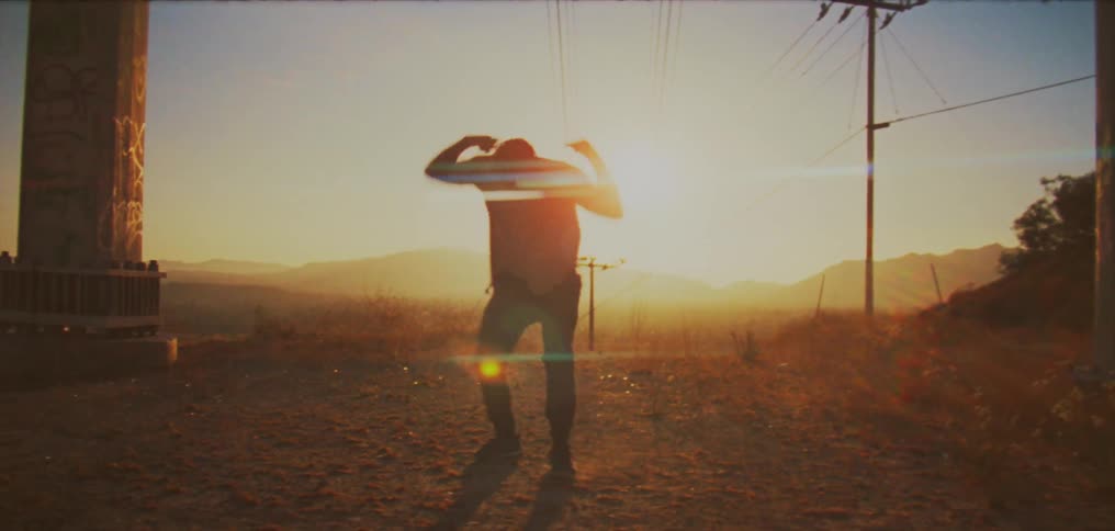 Sun shines behind the silhouette of a man dancing between two poles in the countryside at sunset