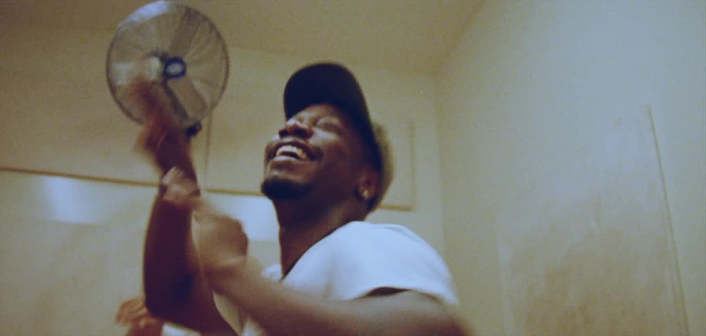 Man with cap earrings necklace and white shirt dances in room laughing