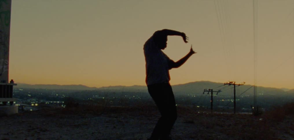 Silhouette of a young man dancing on the countryside near a town at evening