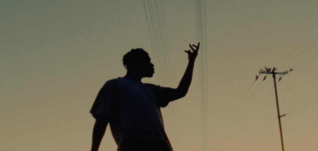 The silhouette of a young man dancing moving his arm and hand rhythmically against a golden sky