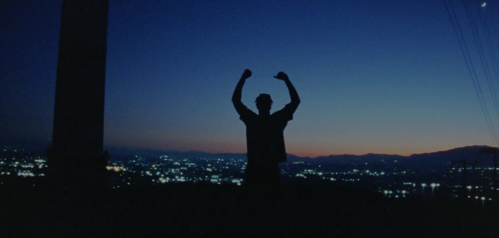 Silhouette of a young man dancing on the countryside near a town at evening