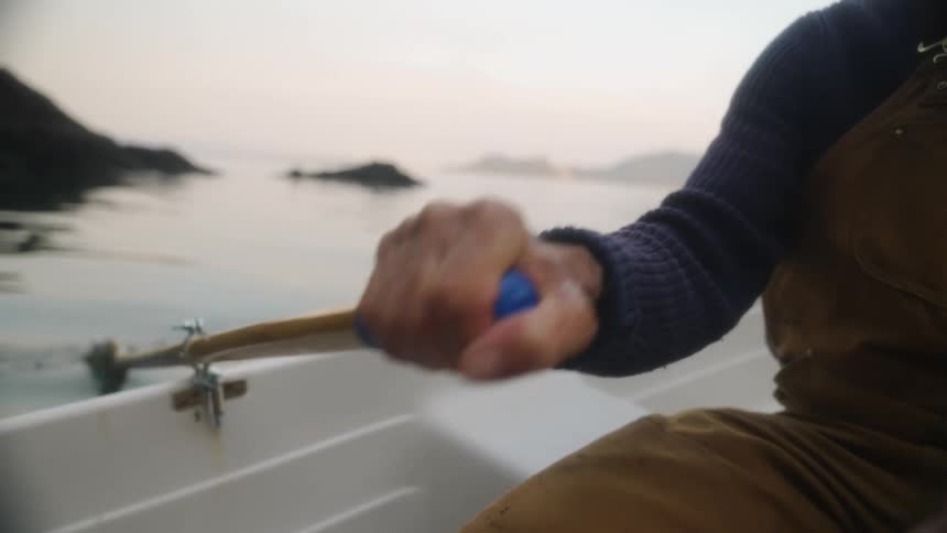 A man rows a boat along the coast on a foggy morning