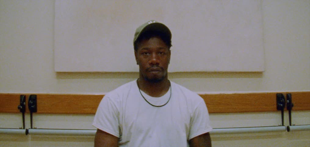 A man wearing a white tshirt and a cap is sitting alone on a bench