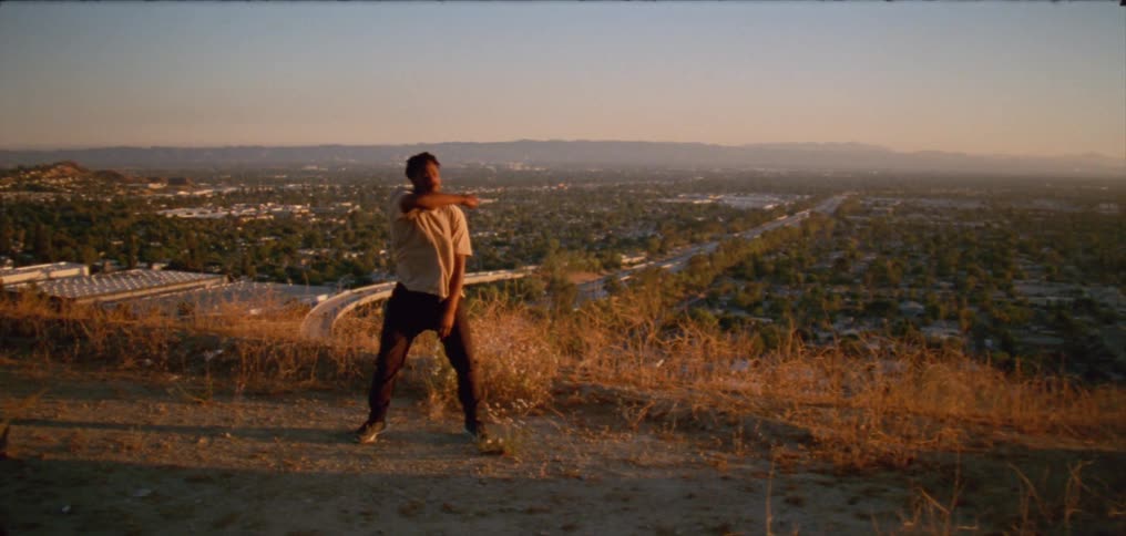 Man dances on hill overlooking town stretching to misty mountains on the horizon