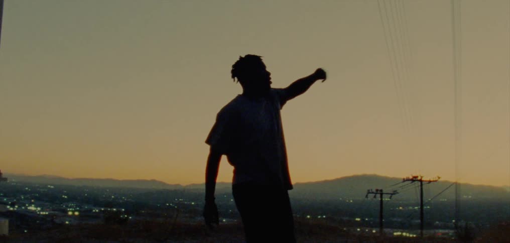 Silhouette of a young man dancing on the countryside near a town at evening