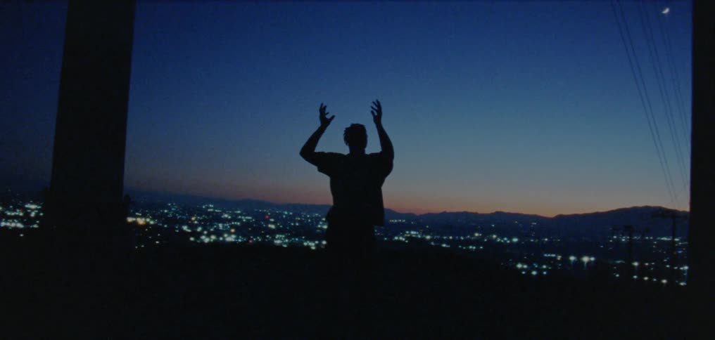 Silhouette of a young man dancing on the countryside near a town at evening