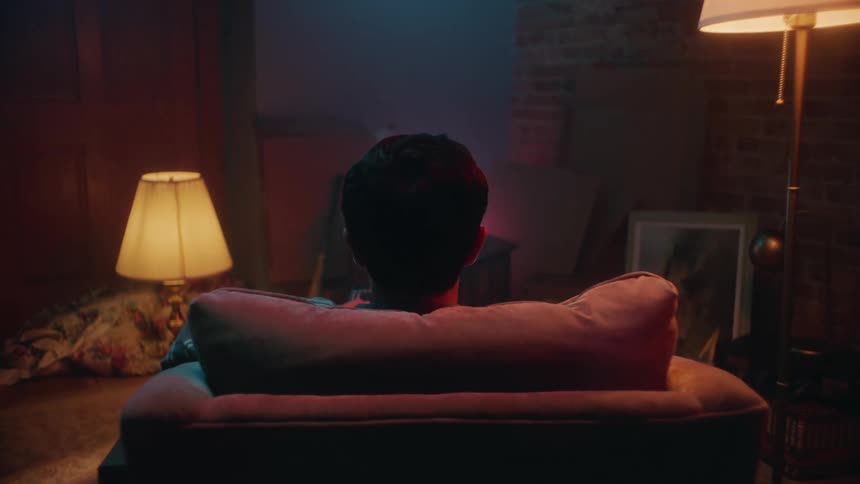 The back of the head of a man sitting in an armchair holding a tv remote