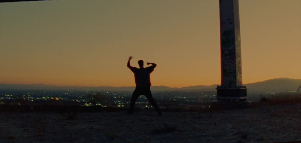 Male dancer silhouetted against the red sky dances near column set on hill overlooking foggy city