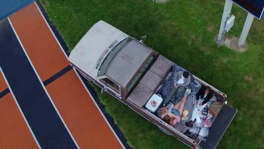 A group of people relax together in bed of a truck parked outdoors during the day