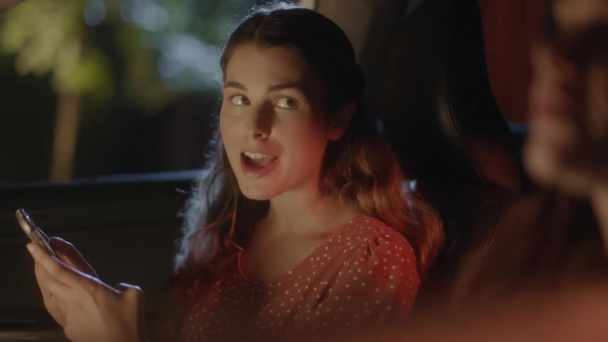 Teenager with a phone in her hands sitting on the passenger seat of a car parked at night talks to the pilot