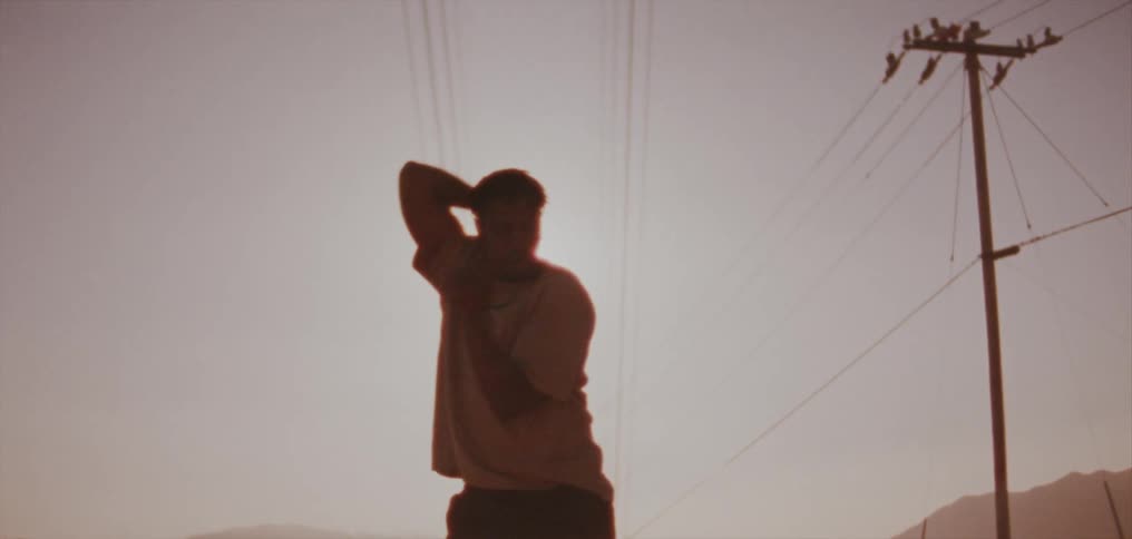 A man is outside dancing outside under utility wires and waving his arms in the air
