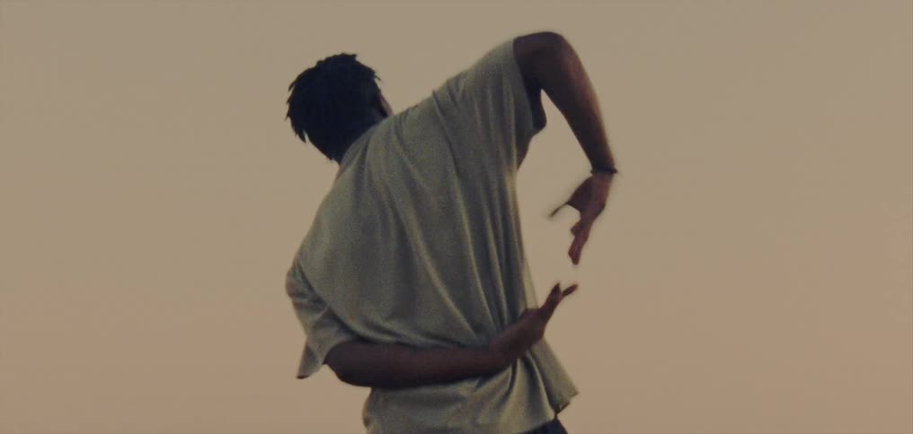 Young man wearing a white shirt dancing on a hill near the foggy mountains at evening