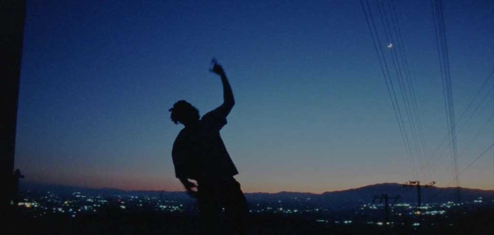 A man dances on a vantage point overlooking a suburb