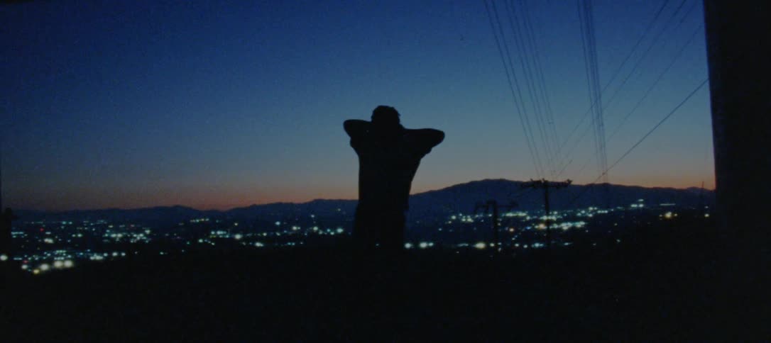 Male dancer dances silhouetted against red tinted horizon and brightly lit city scape