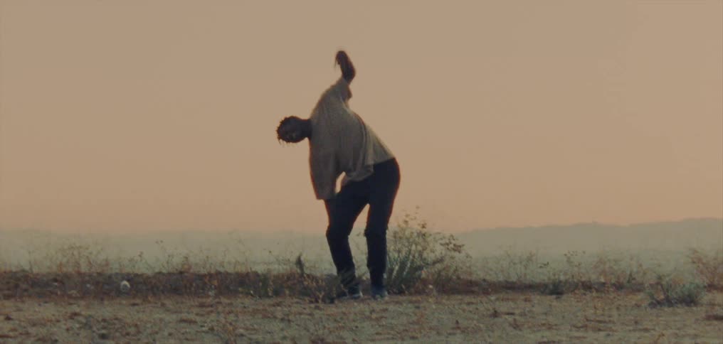 Young man wearing a white shirt dancing on a hill at evening
