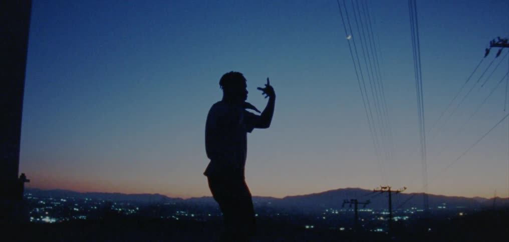 Silhouette of a young man dancing on the countryside near a town at evening