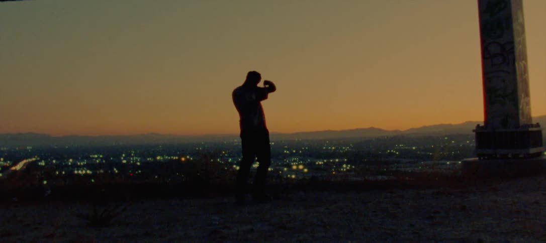A man dances on an overpass overlooking a neighborhood at night