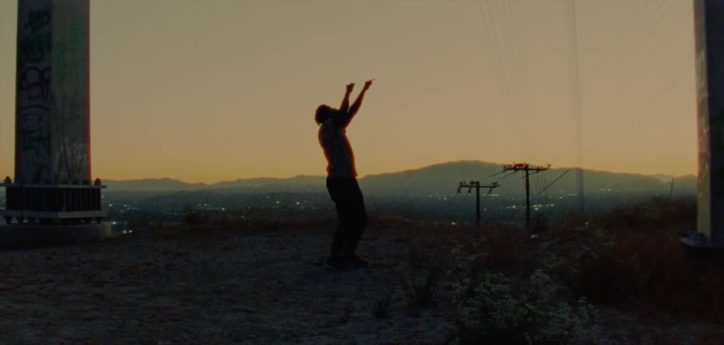 The silhouette of a young man dancing on a ridge against a golden sky