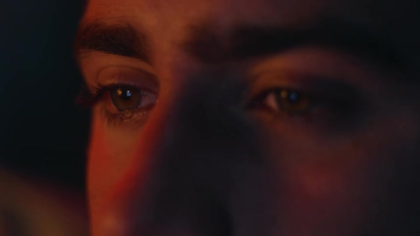 A red light shines on the face of a woman who is blinking her eyes and looking around