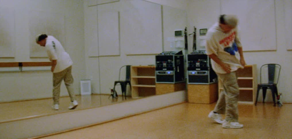 Young happy man wearing a white shirt dances alone energetically in front of a mirror