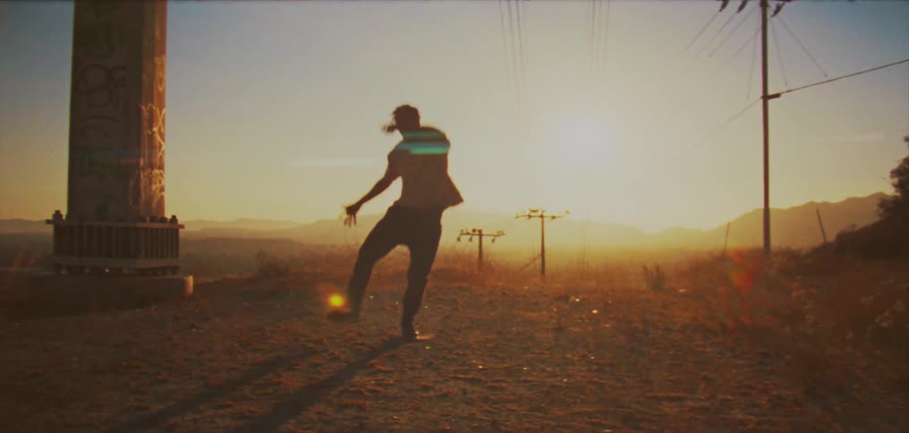 Sun shines behind the silhouette of a man dancing between two poles in the countryside at sunset
