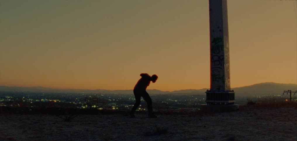 Male dancer dancing is silhouetted against the red sky in the country at dusk