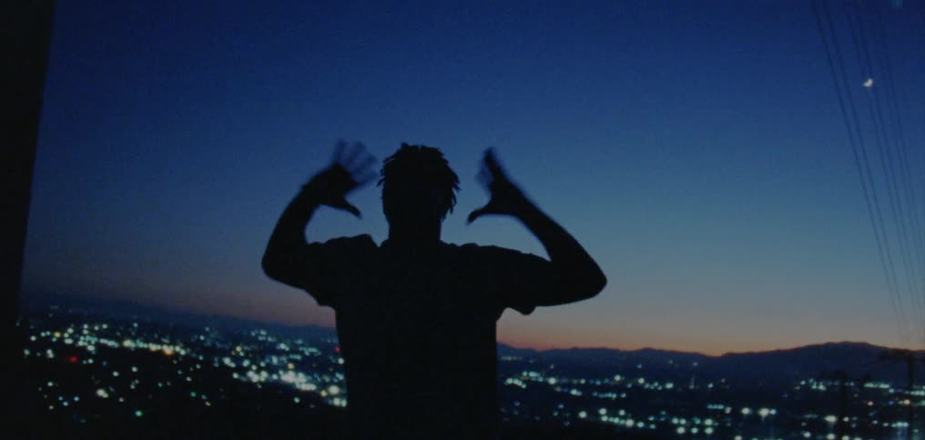 A man dances in front of a skyline at night