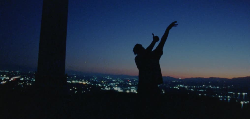 Silhouette of a young man dancing on the countryside near a town at nightfall