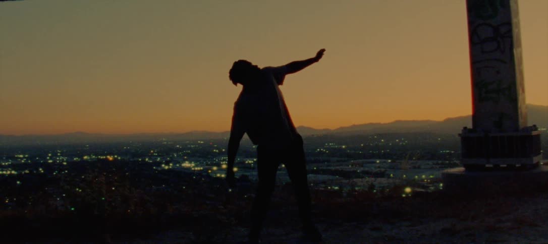 Silhouette of a young man dancing on the countryside near a town at evening