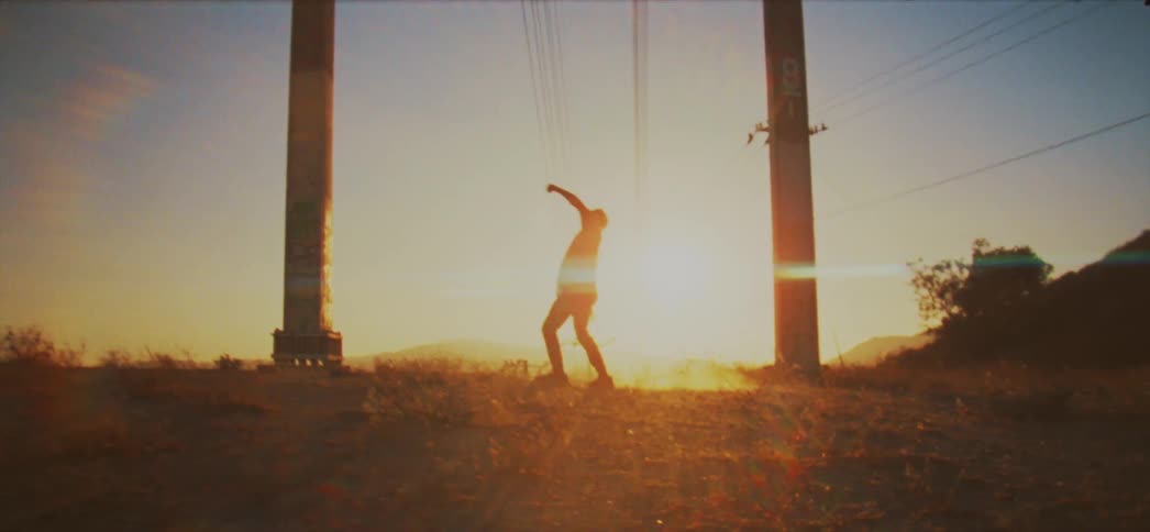 Male dancer dances between columns while backlit by sun shining from the horizon