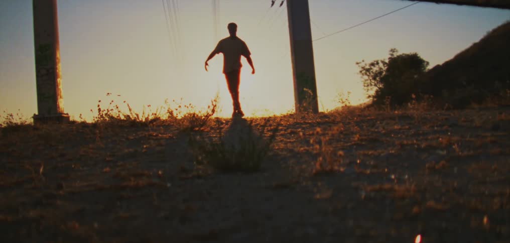Sun shines behind the silhouette of a man dancing between two poles in the countryside at sunset