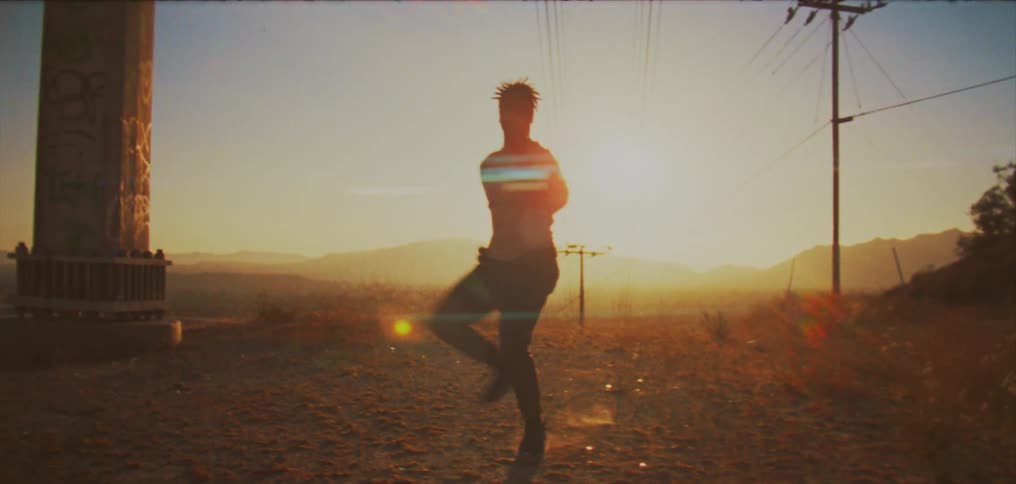 A young man jumping and dancing as the sun glares behind him