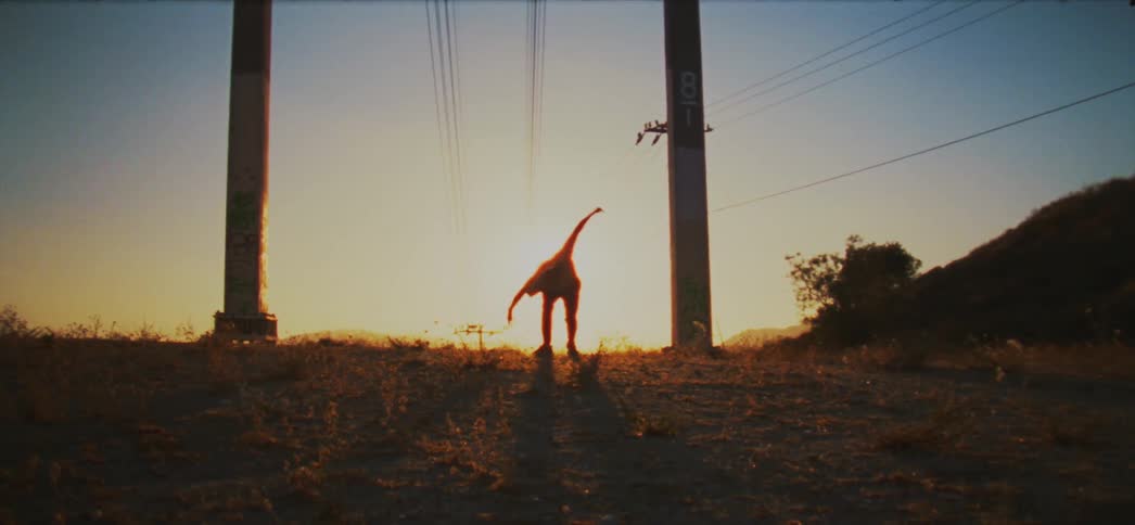 Silhouette of a man dancing between pillars with electrical wires hanging overhead and the sun on the horizon