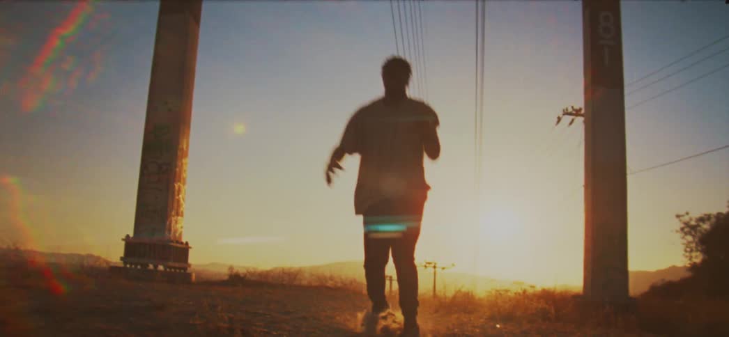 A man dances in a field with utility poles