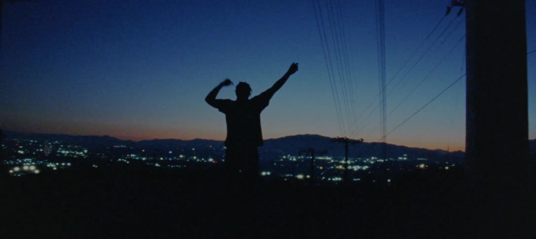 Silhouette of a young man dancing on the countryside near a town at evening
