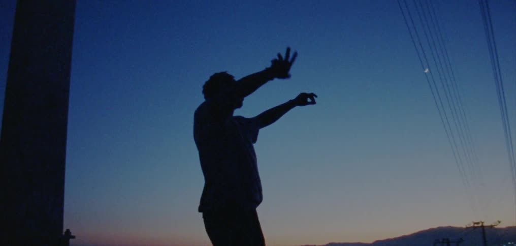 Silhouette of a young man dancing on the countryside near a town at nightfall