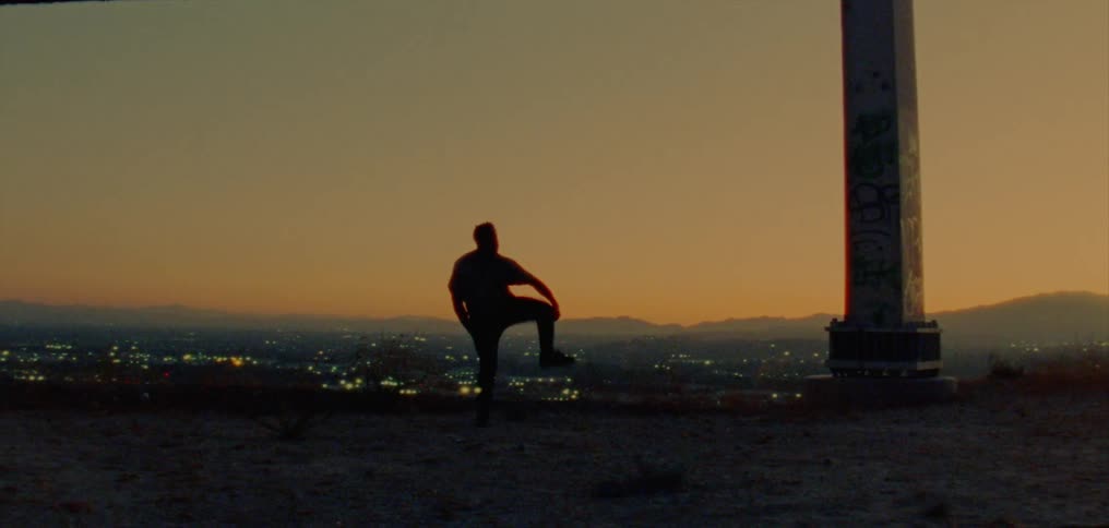 Silhouette of a young man dancing on the countryside near a town at evening