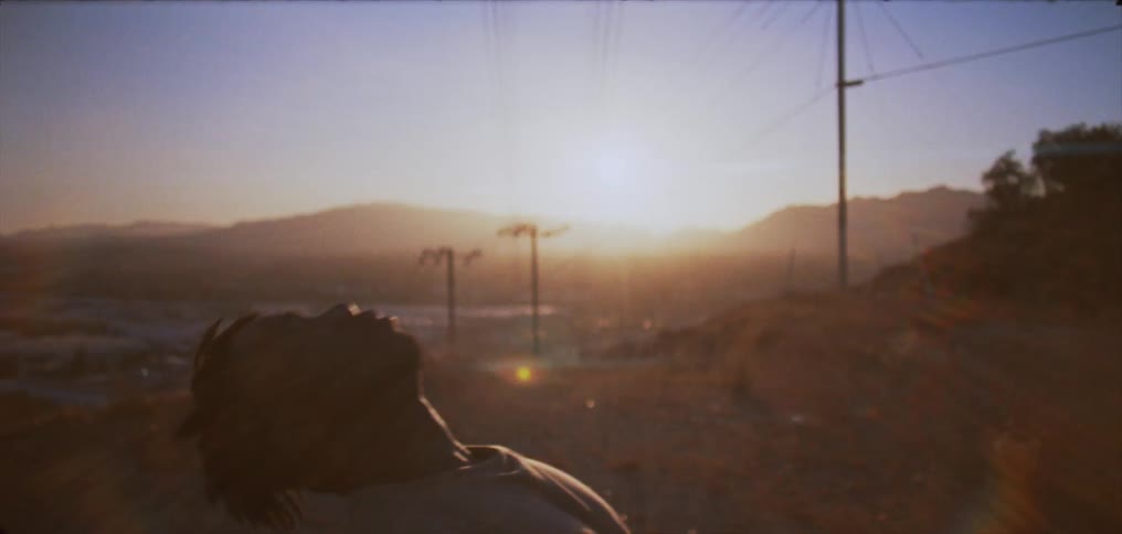 A man stands in a field lined with utility poles and leans his body backwards