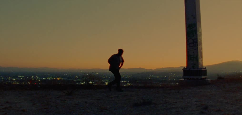 A man dances hip hop style on a vantage point overlooking a suburb