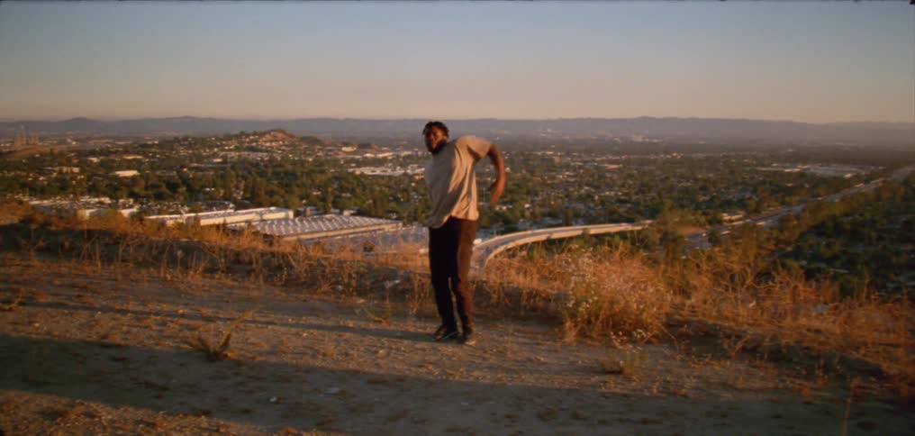 A man dances on a hill overlooking a freeway in the evening
