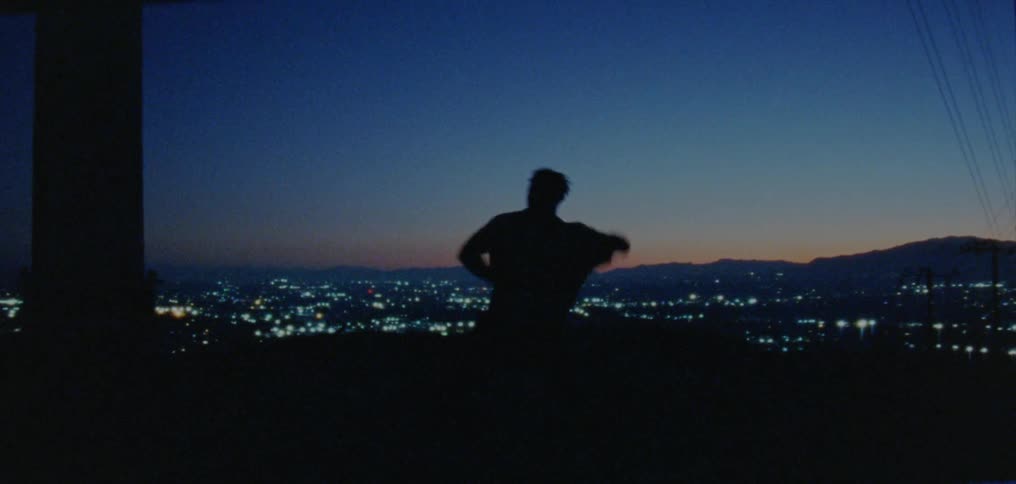 Silhouette of a young man dancing on the countryside near a town at nightfall