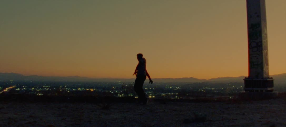 The silhouette of a young man dancing standing on a ridge overlooking city lights