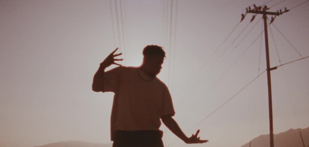 The sun shines down on a man as he dances next to a utility pole