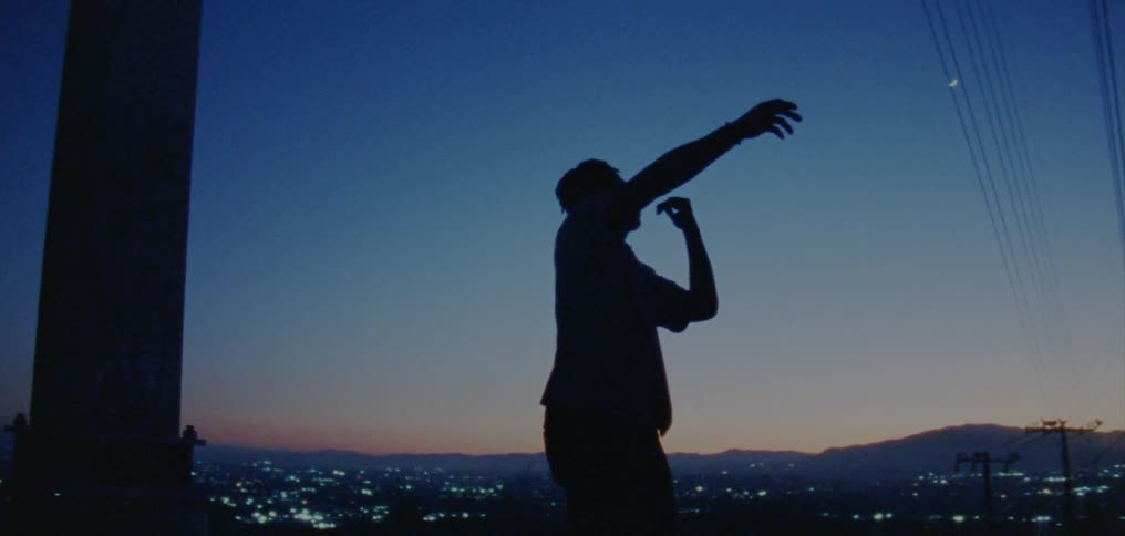 Male dancer silhouetted against red tinted horizon and city scape at night dances