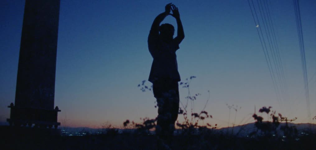 Silhouette of a young man dancing on the countryside near a town at nightfall