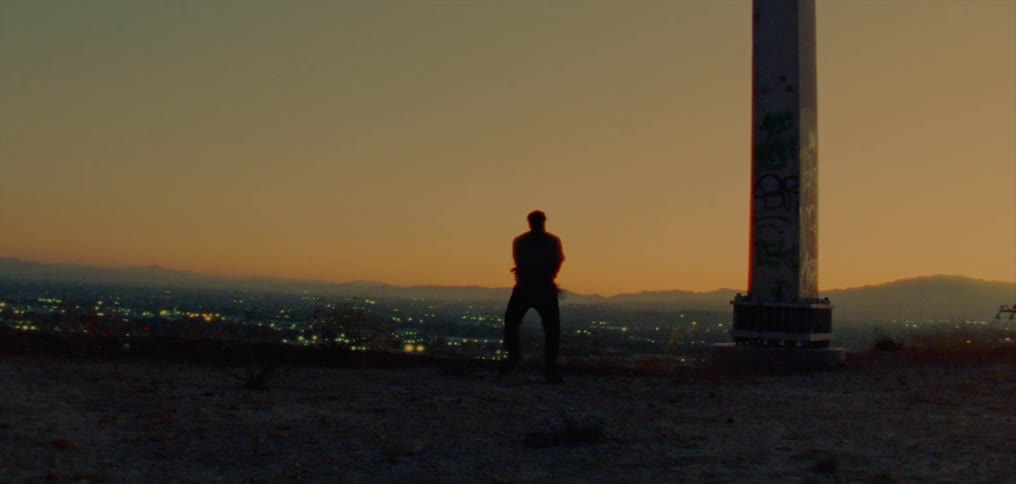 Male dancer silhouetted against night sky dance near support set on hill overlooking city