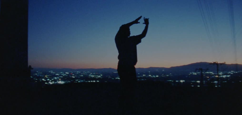 Silhouette of a young man dancing on the countryside near a town at nightfall