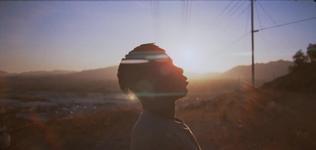 Sunlight behind the silhouette of a man standing on a hill in the countryside reclining back
